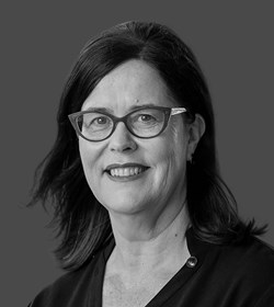 Headshot of Veronica Jeffrey - a women with red glasses, dark brown hair who is smiling against a leafy green background